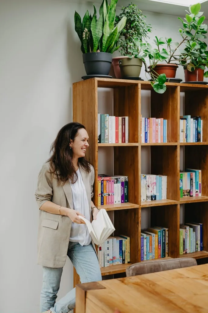 Madelon met een open boek in haar handen, bij een boekenkast vol kleurige romans